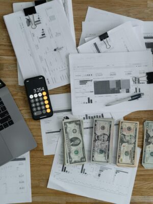 Overhead view of financial documents, cash, and technology on a wooden desk.